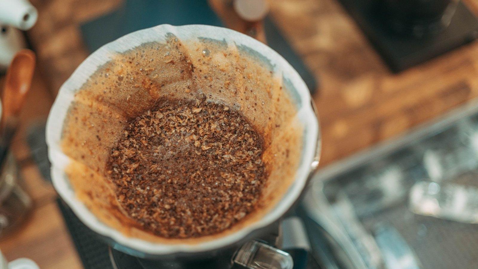 A close-up of wet coffee grounds blooming in a white pour over filter as trapped gas escapes